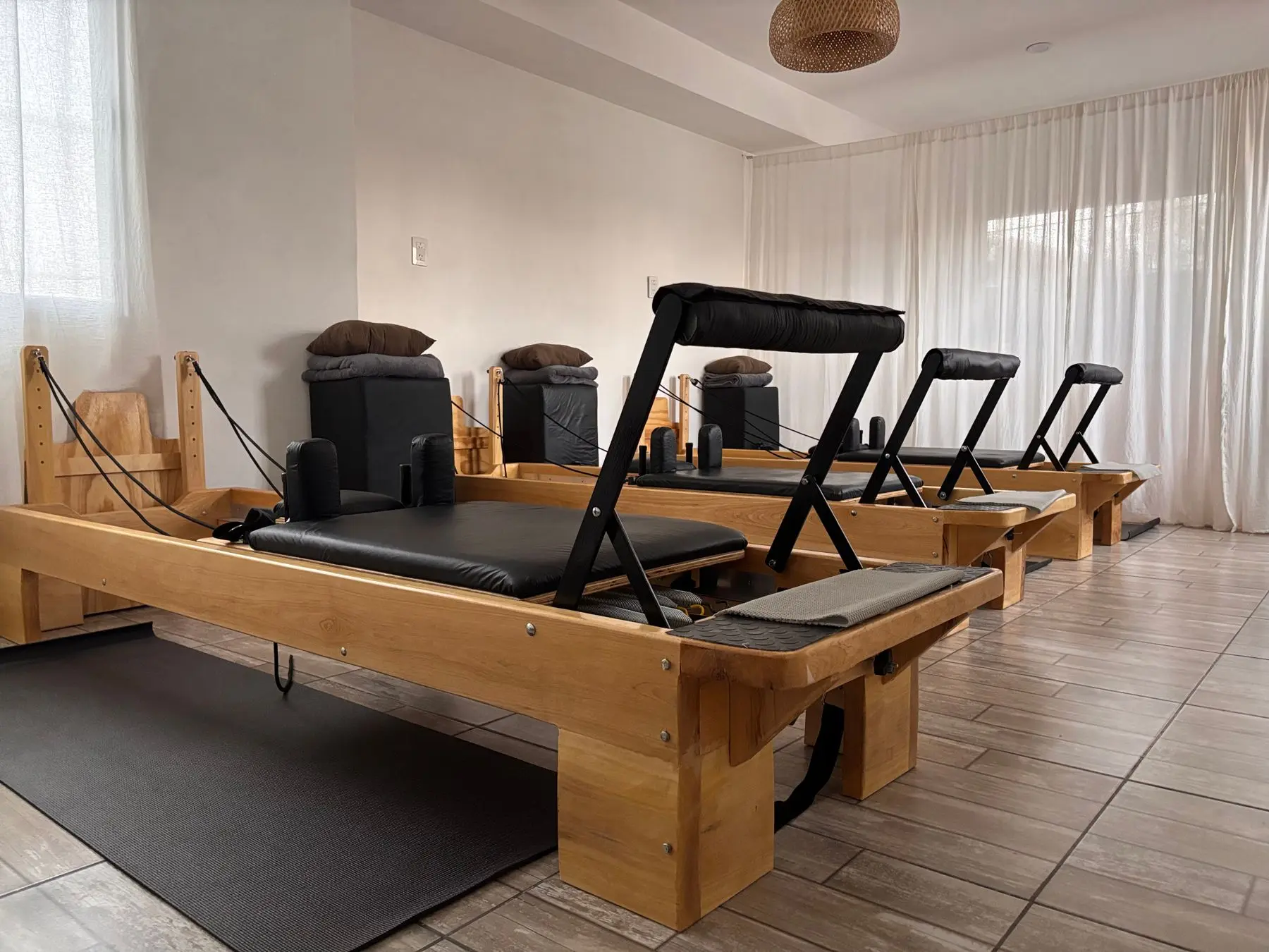 Wooden pilates reformers in a quiet studio with sheer curtains