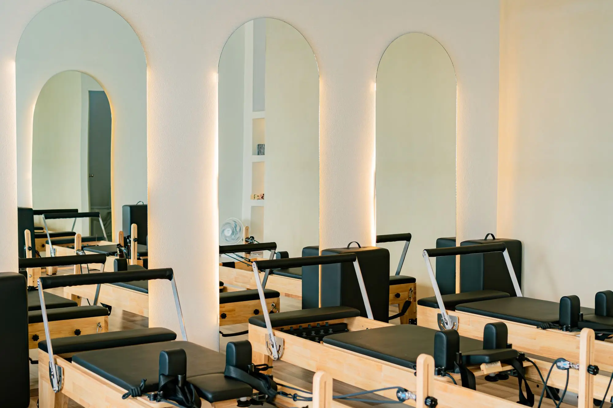 A bright pilates studio with reformer beds set in front of arched mirrors