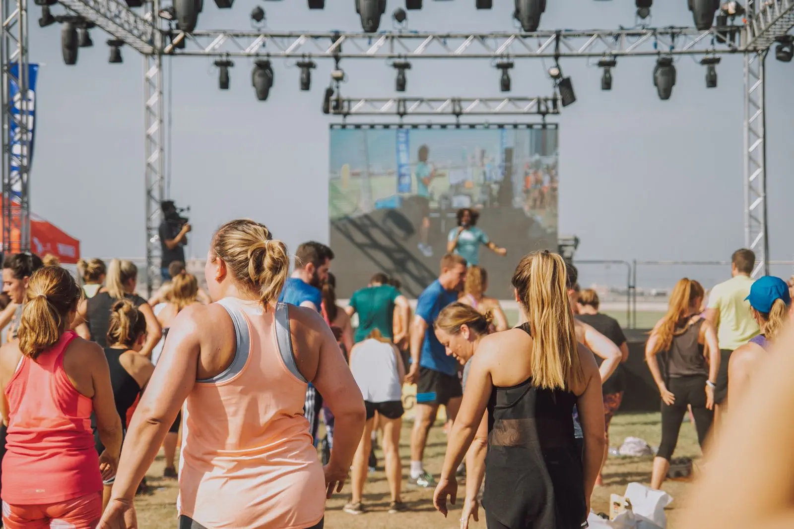 A crowd taking part in an outdoor fitness event in front of a stage