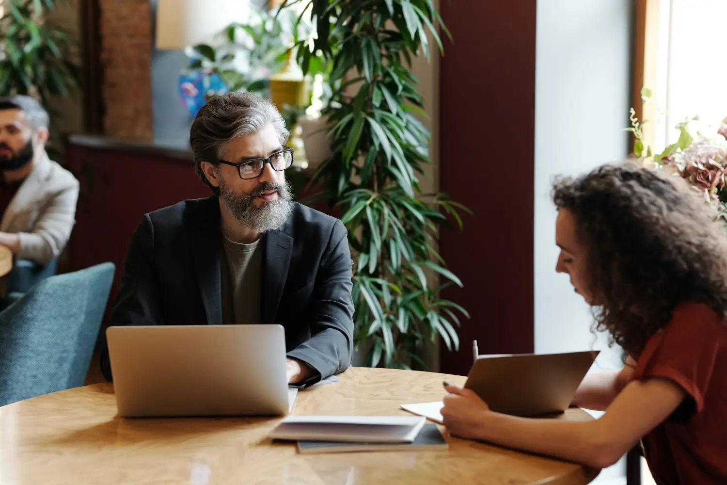 Two people reviewing work over laptops at a wooden table